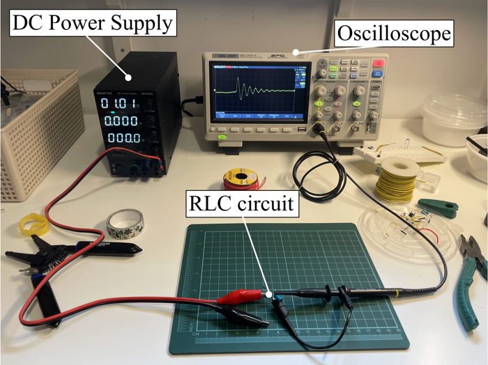 Bench setup: DC power supply, oscilloscope showing a damped ring-down, and a soldered RLC circuit on a cutting mat